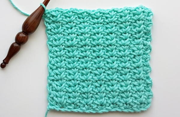 Image shows a crochet hook attached to a swatch of teal yarn made using the spider stitch. Image shows a crochet hook attached to a swatch of teal yarn made using the spider stitch.