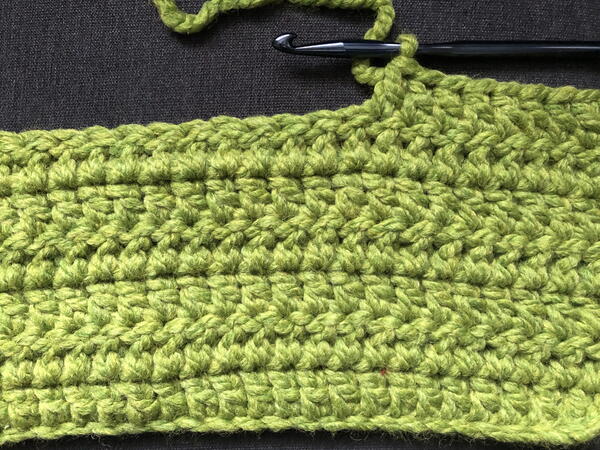 Image shows the start of a double crochet stitch blanket in green. Image shows the start of a double crochet stitch blanket in green.